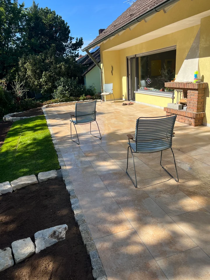Terrasse mit großformatigen hellen Platten, daneben ein Rasenstreifen und frisch angelegte Beete